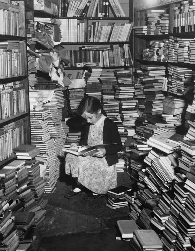 A young girl reading in a cluttered corner of Foyles bookshop, London. 
